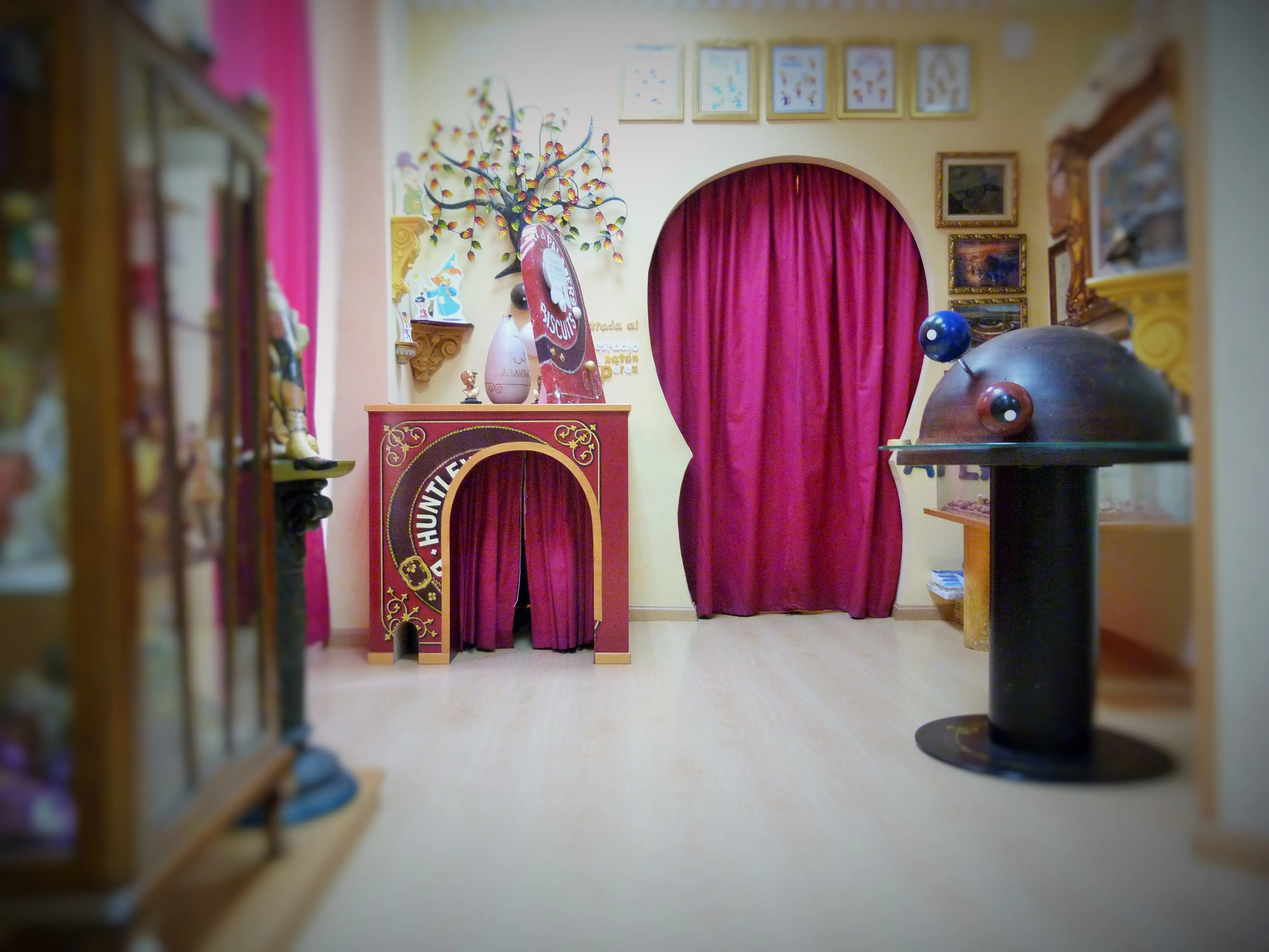 El colorido interior de un museo con un arco cubierto de cortinas rojas, una chimenea decorativa y una gran escultura de ratón metálico.