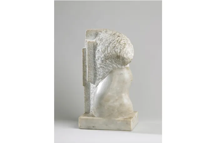 Escultura de piedra blanca que representa una cabeza con cabello rizado texturizado, montada sobre una base rectangular con una placa vertical detrás
