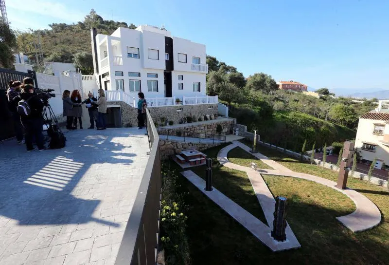 Edificio blanco de varias plantas con un jardín esculpido que presenta senderos sinuosos y esculturas al aire libre, con personas y un equipo de rodaje en una terraza.