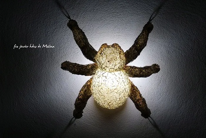Escultura de araña con cuerpo brillante y texturizado y patas oscuras colgada en una pared
