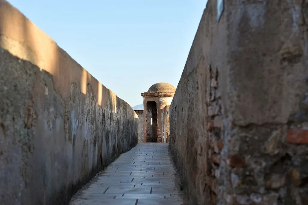 Un estrecho sendero empedrado entre dos altos muros de la fortaleza que conduce a una pequeña garita abovedada en el Castillo de Gibralfaro