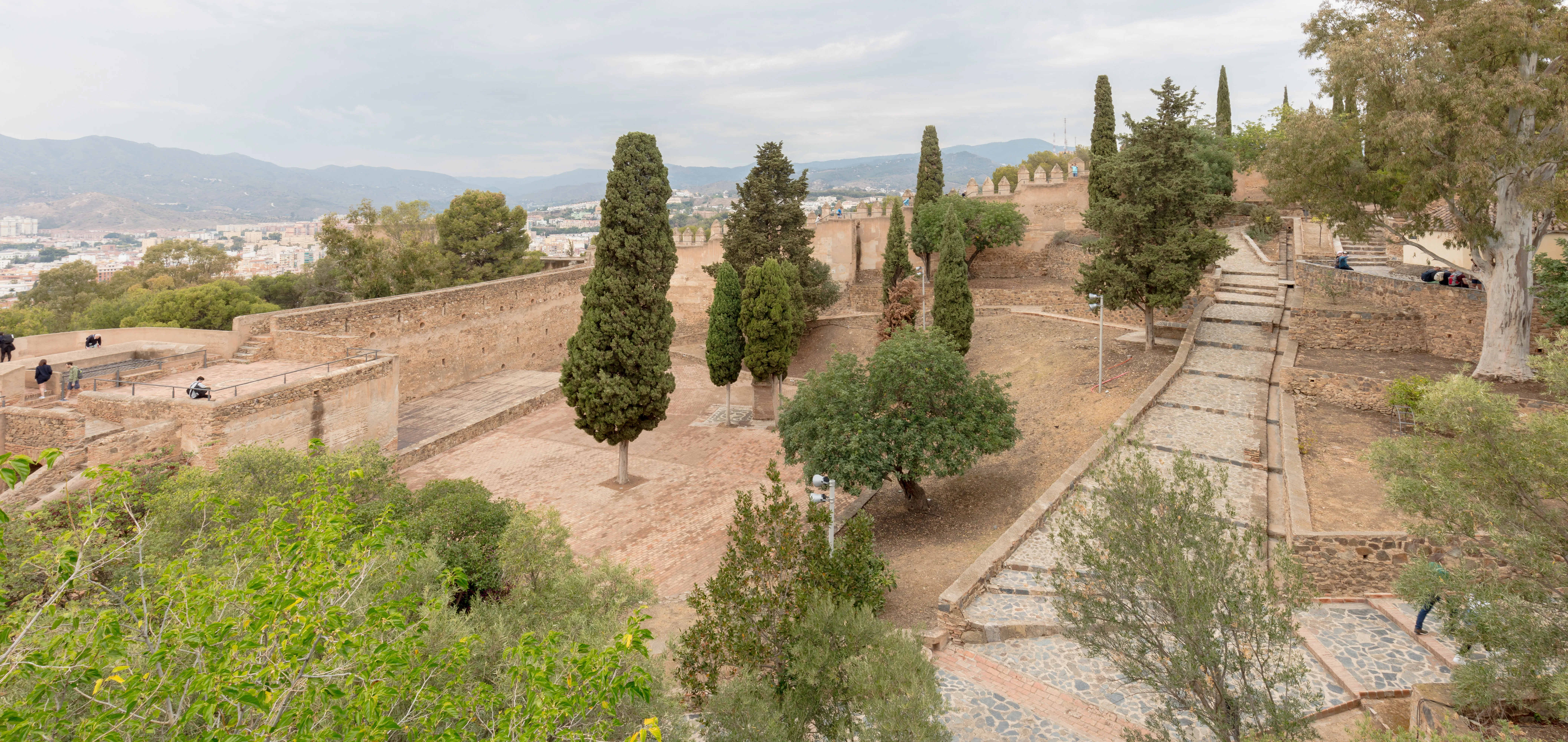 Vista panorámica del recinto del Castillo de Gibralfaro con sus murallas de piedra, cipreses, senderos y la ciudad de Málaga con las montañas al fondo