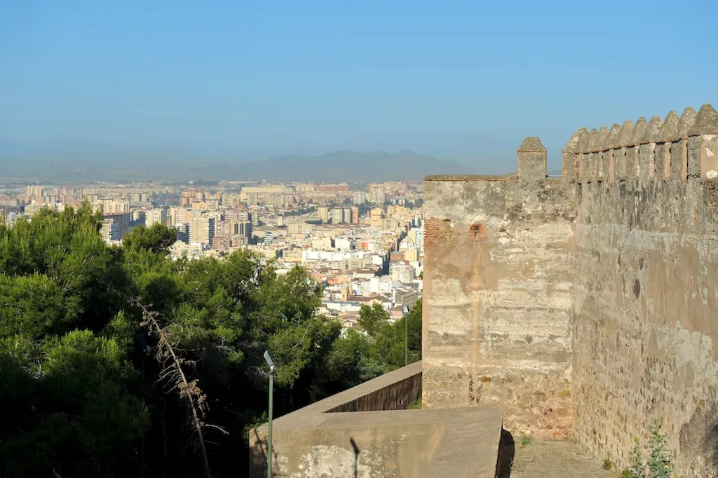 Muros de piedra almenados del Castillo de Gibralfaro con vistas a la ciudad de Málaga y a la costa mediterránea bajo un cielo azul despejado