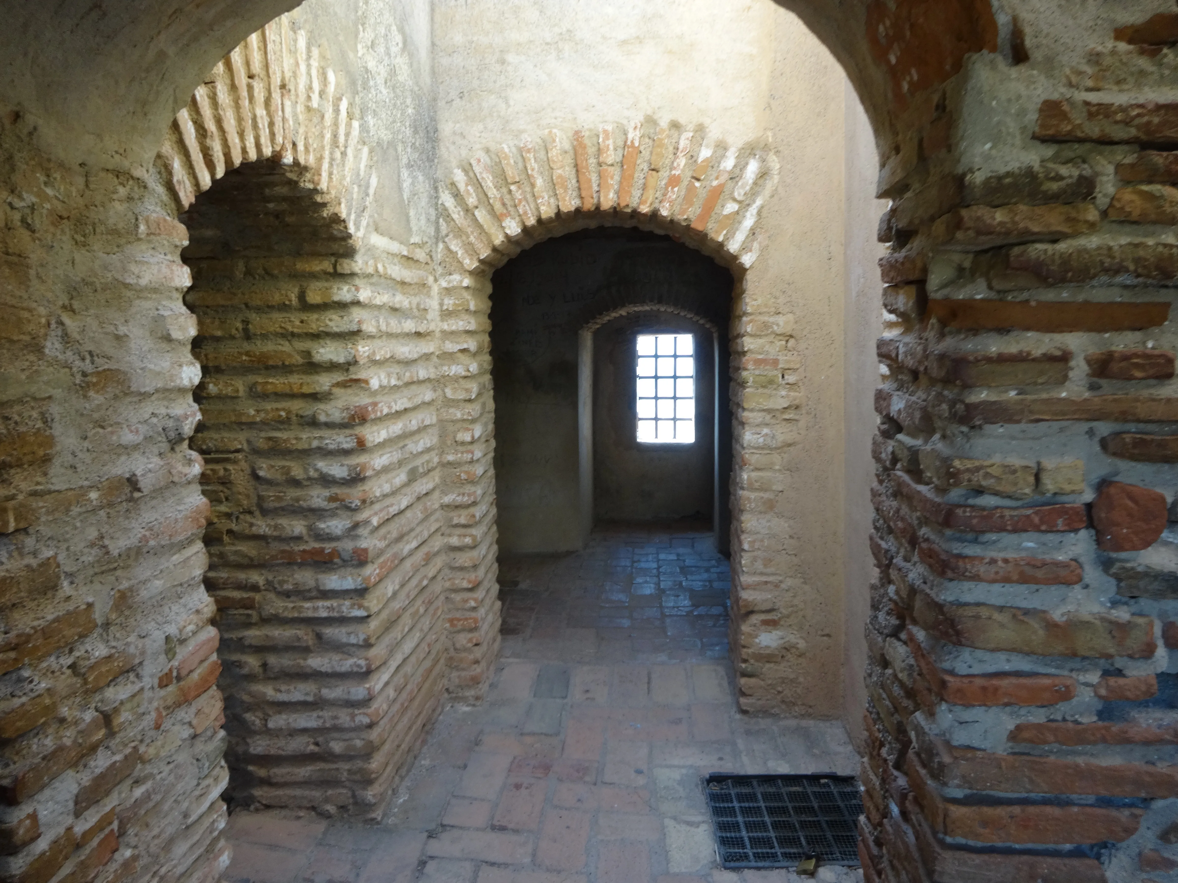 Pasillo interior de un castillo histórico con arcos de ladrillo y suelo de piedra que conduce a una ventana al fondo