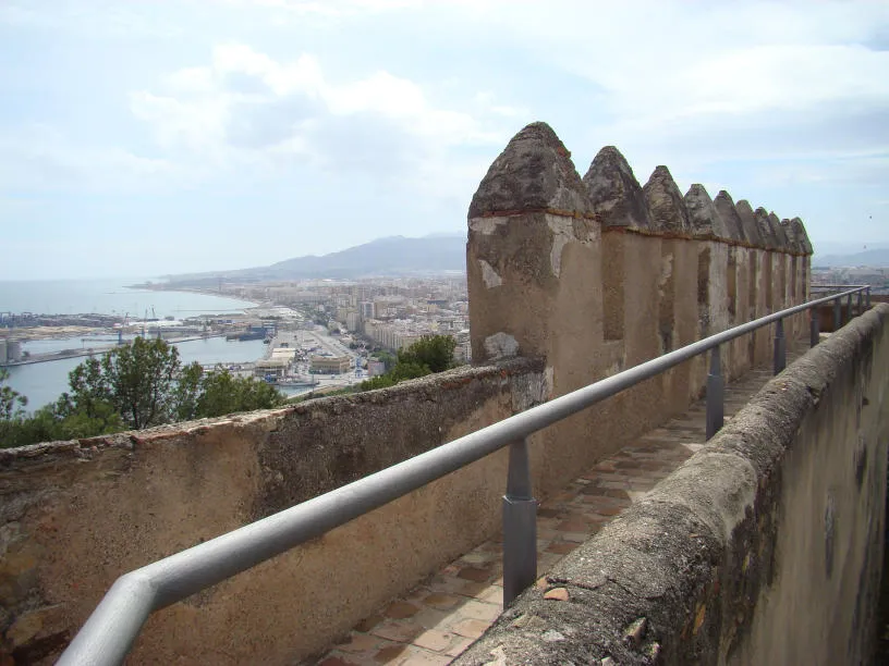 Murallas del castillo con almenas y barandilla de metal con vistas a la ciudad de Málaga, el puerto y la costa mediterránea