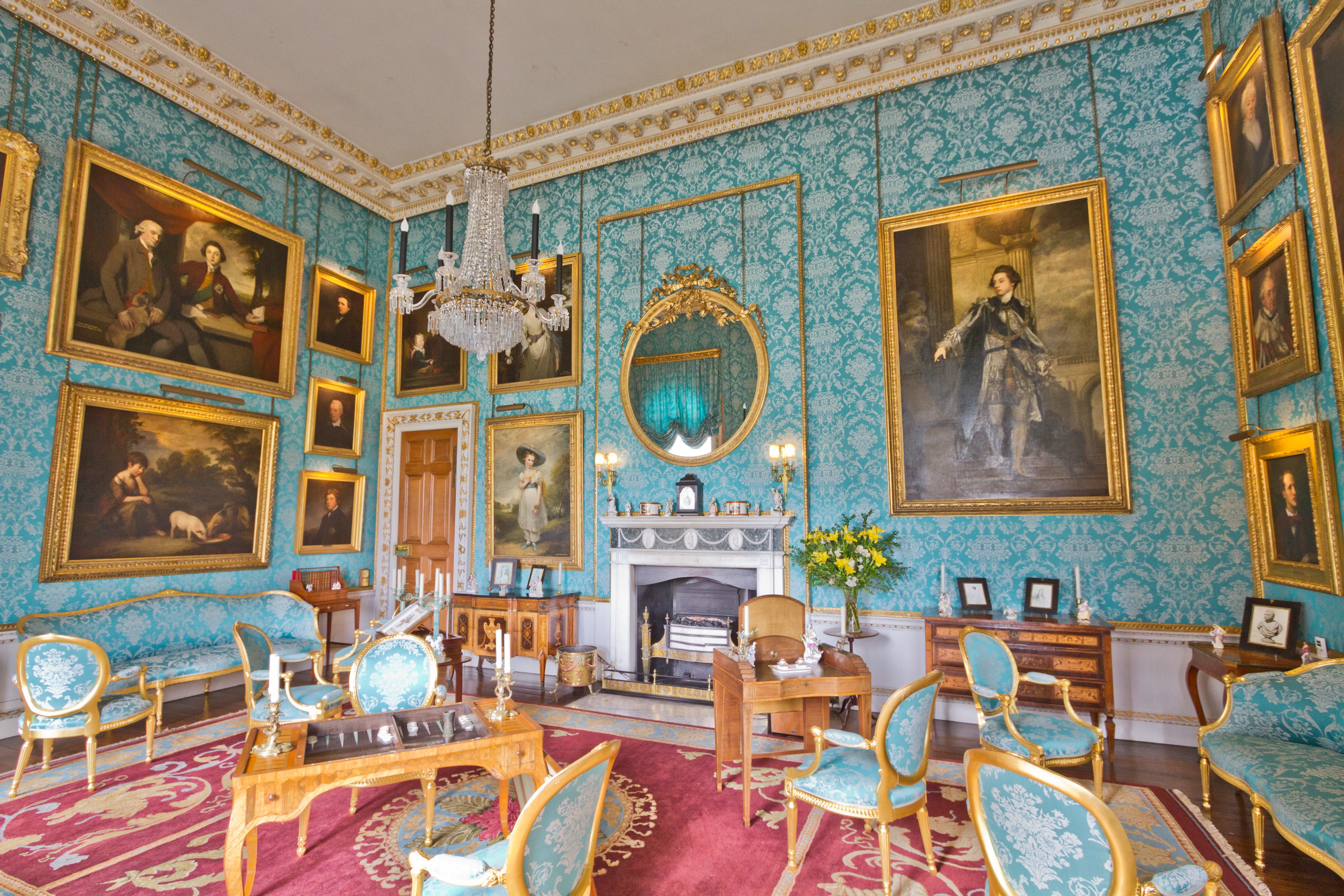 Grote salon met turquoise muren met patroon, portretten in vergulde lijsten, kristallen kroonluchters, een marmeren schouw en blauw gestoffeerde meubels