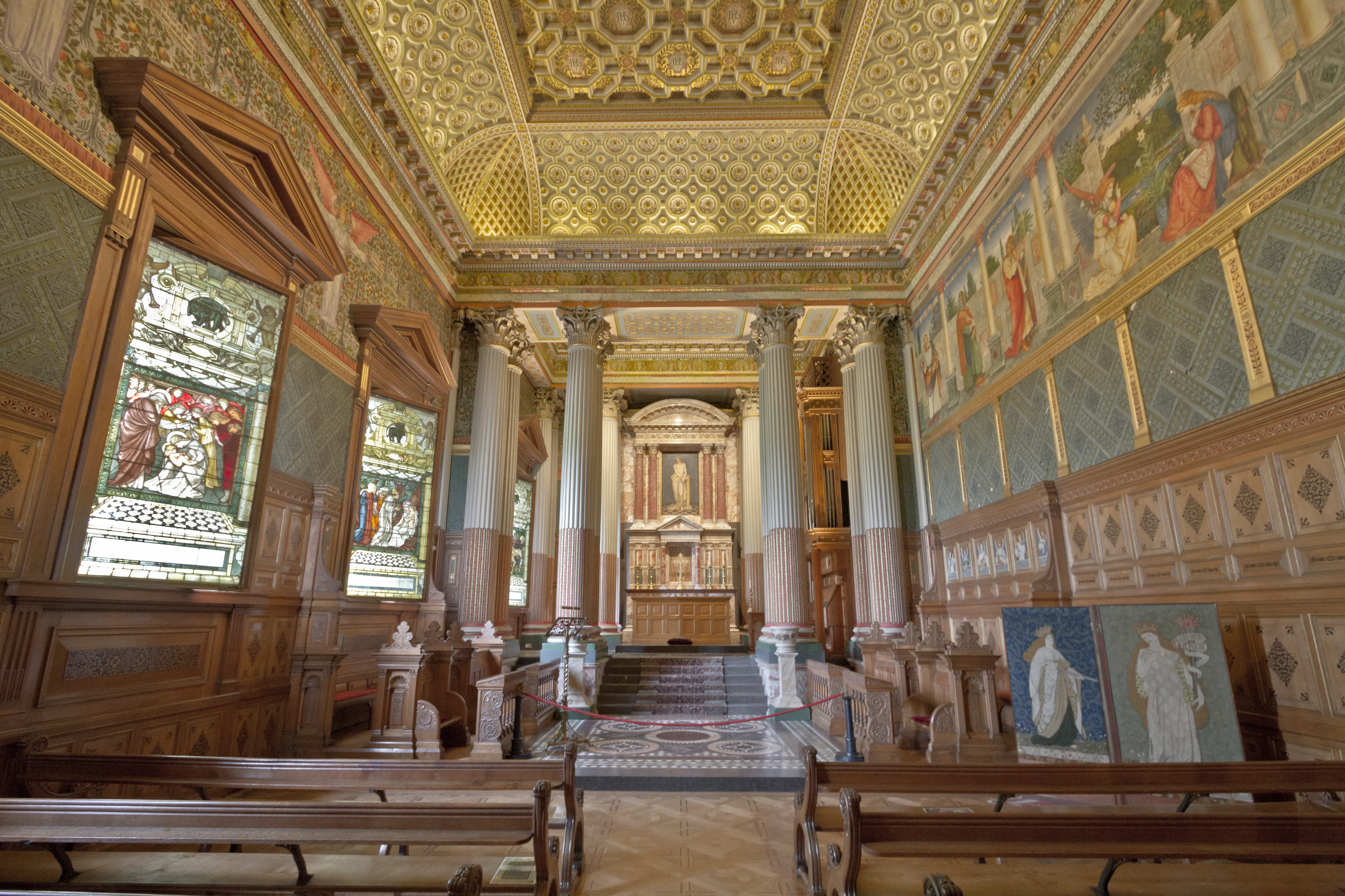 Interieur van de kapel van Castle Howard met een sierlijk goudkleurig cassettenplafond, marmeren zuilen, houten kerkbanken, glas-in-loodramen en beschilderde wandpanelen.
