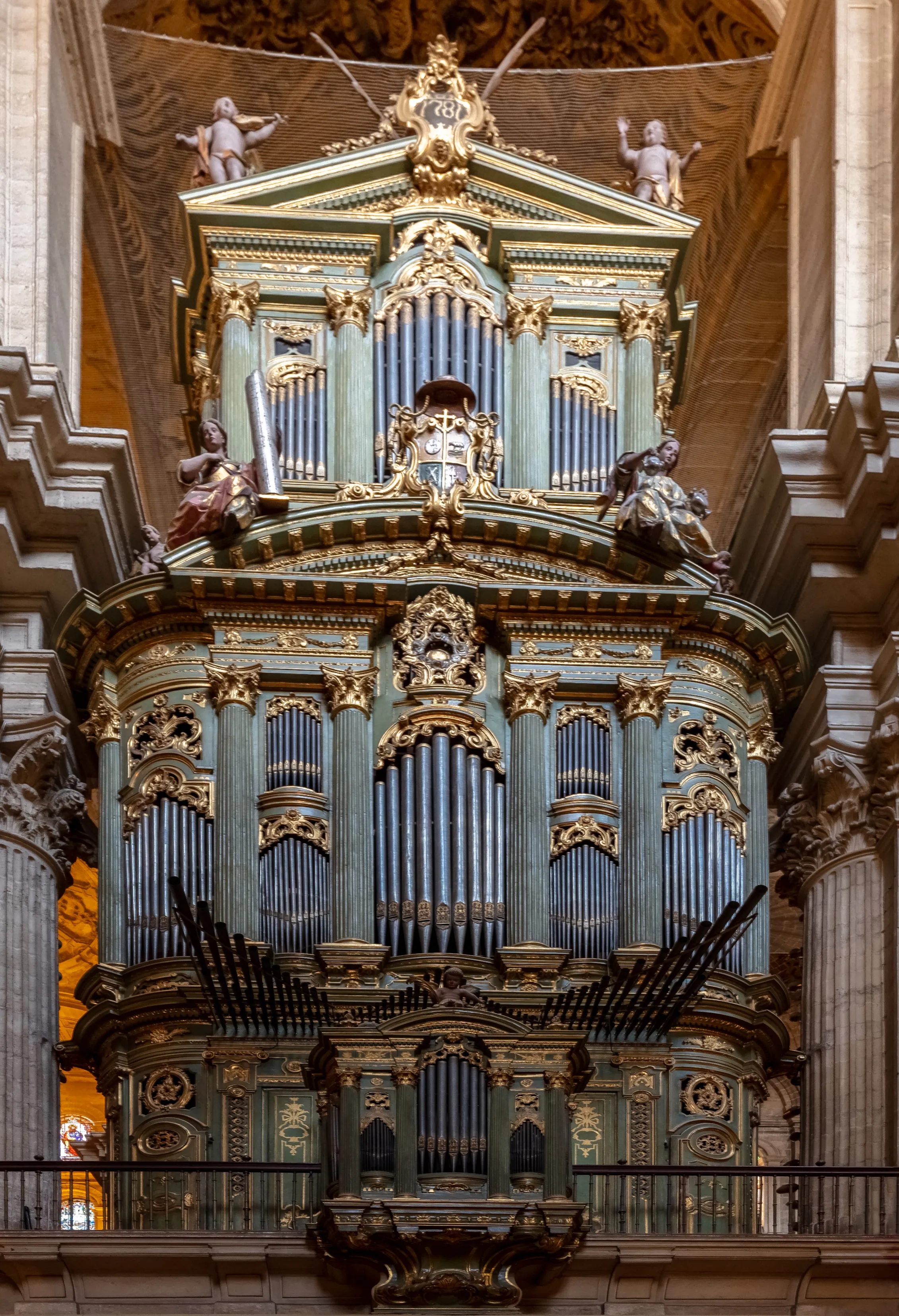 Ornato órgano barroco de tubos dentro de una catedral con carpintería en color verde azulado, decoraciones doradas, figuras escultóricas de ángeles en la parte superior y varias filas de tubos de metal dispuestos en una estructura de varios niveles