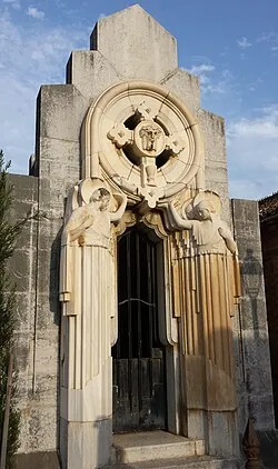 Stenen mausoleumgevel met een cirkelvormig reliëf met een kruis en flankerende engelfiguren boven een boogdeur met ijzeren hek