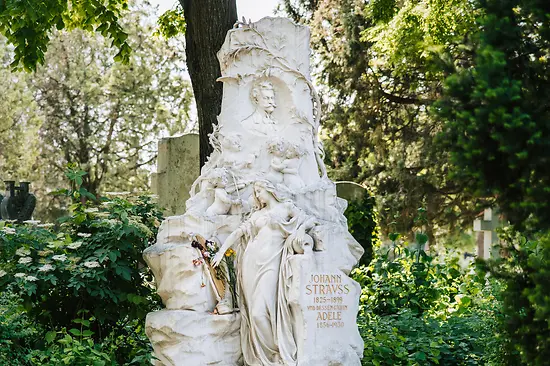 White marble monument with sculpted figures and inscriptions in a cemetery setting