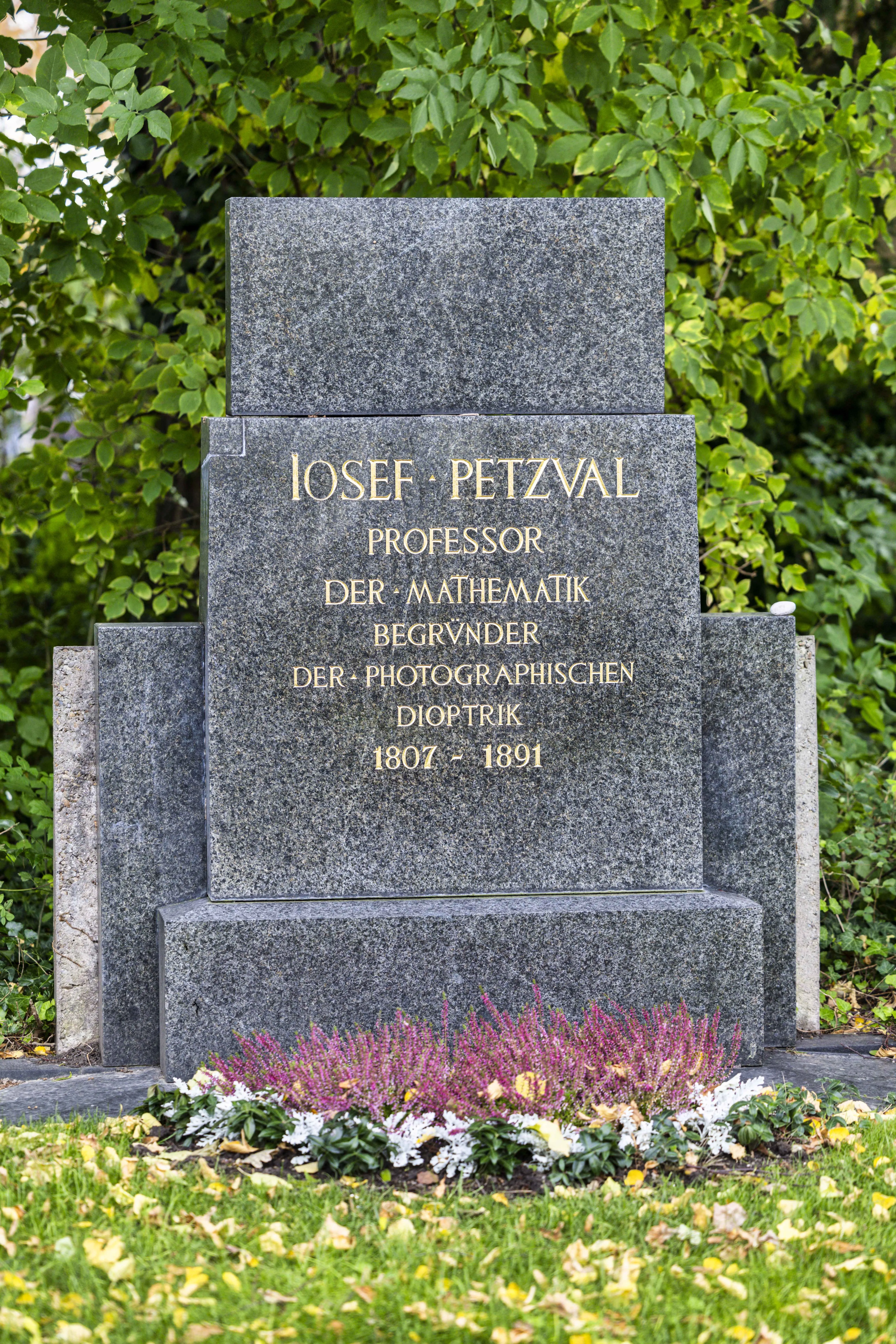 Grave marker for Josef Petzval with gold lettering on dark stone, surrounded by flowers and greenery