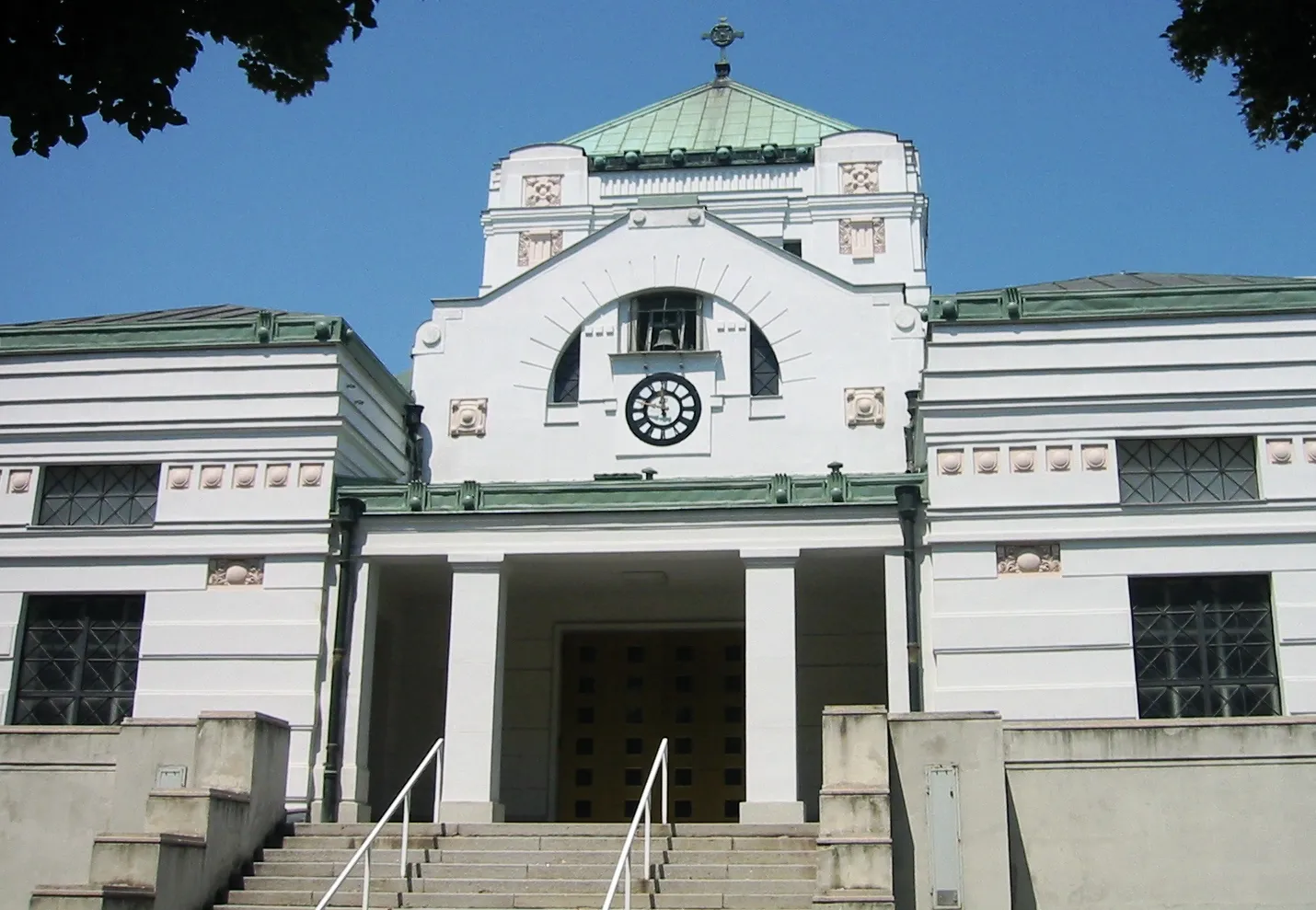 White Art Nouveau building with green roof and central clock at Central Cemetery entrance