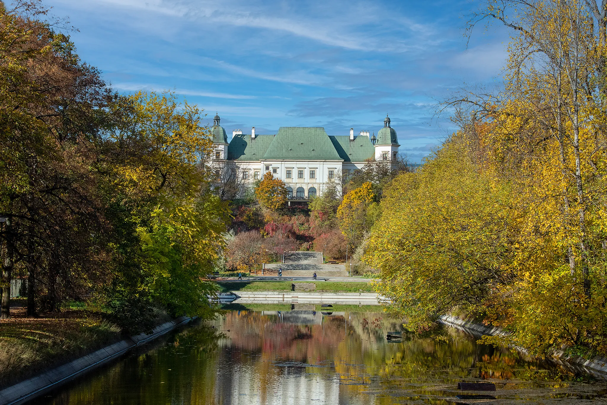 Castillo Ujazdowski con techo verde rodeado de árboles de otoño y un canal que refleja el edificio