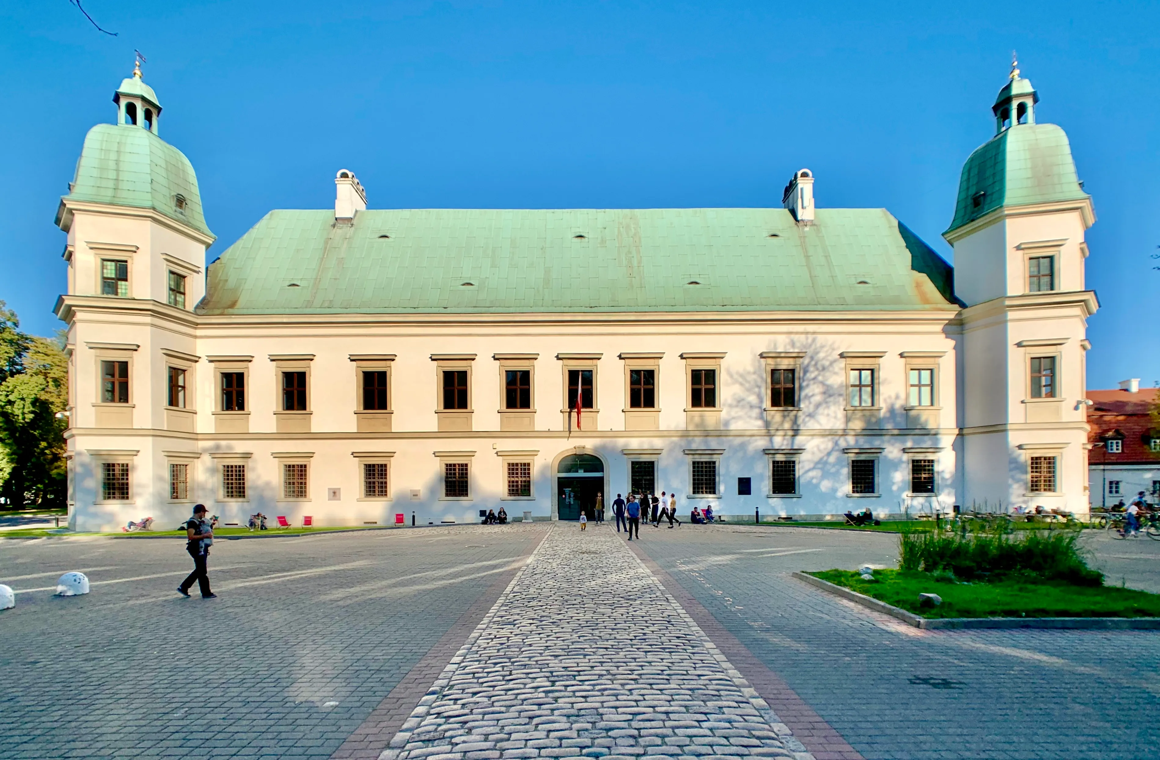 Castillo Ujazdowski con torres de cúpula verde y un patio adoquinado bajo un cielo azul claro