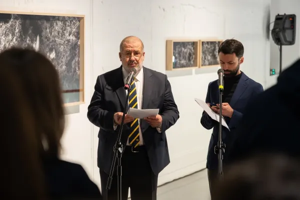 Twee mannen die aan microfoons spreken in een kunstgalerie met ingelijste kunst aan de muren