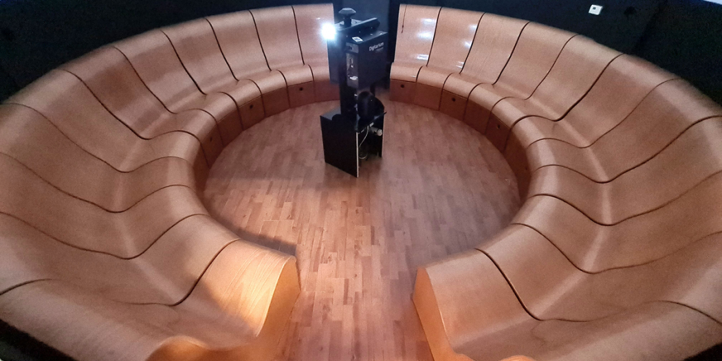 Bancos de madera curvados y escalonados dispuestos en forma circular dentro del auditorio de un planetario