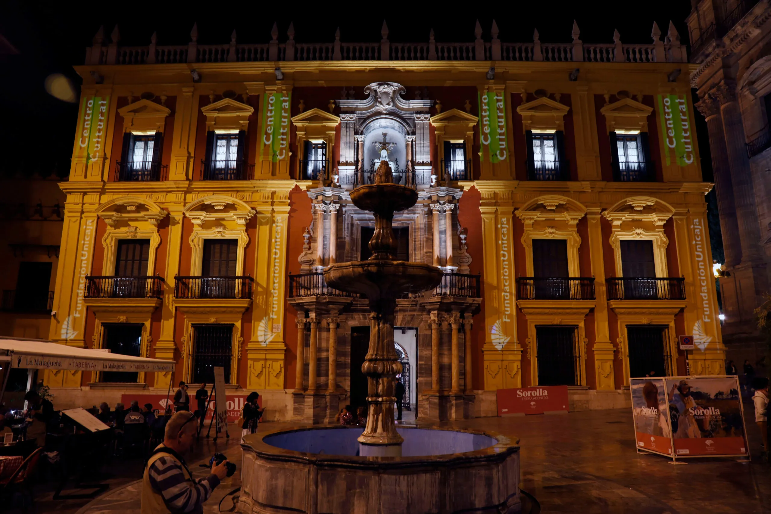 Fachada de un palacio barroco iluminado por la noche con una fuente de piedra ornamentada en la plaza frontal