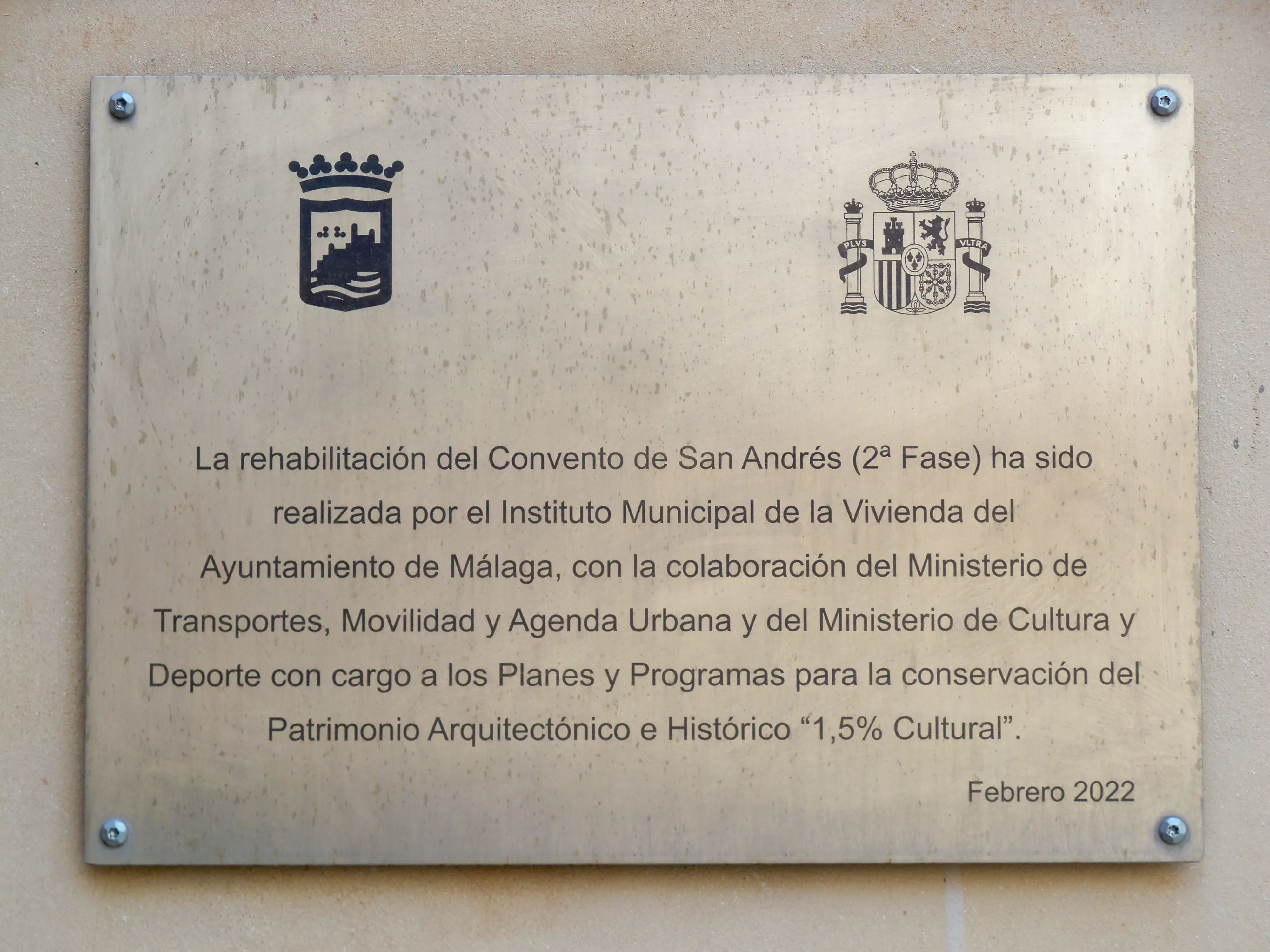 Placa de metal montada sobre una pared de color beige que presenta los escudos de armas de Málaga y España, con un texto en español que detalla la rehabilitación del Convento de San Andrés en 2022.