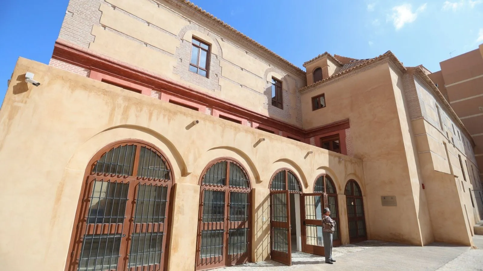 Fachada exterior del Centro de Interpretación Histórico José María Torrijos con grandes puertas de madera arqueadas con rejas de hierro y un acabado de estuco beige bajo un cielo azul.
