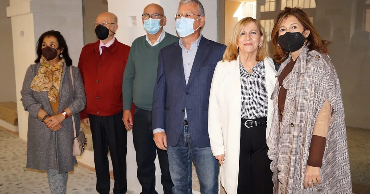 Seis personas con mascarillas de pie juntas en fila en un interior, vestidas con atuendo formal y semiformal