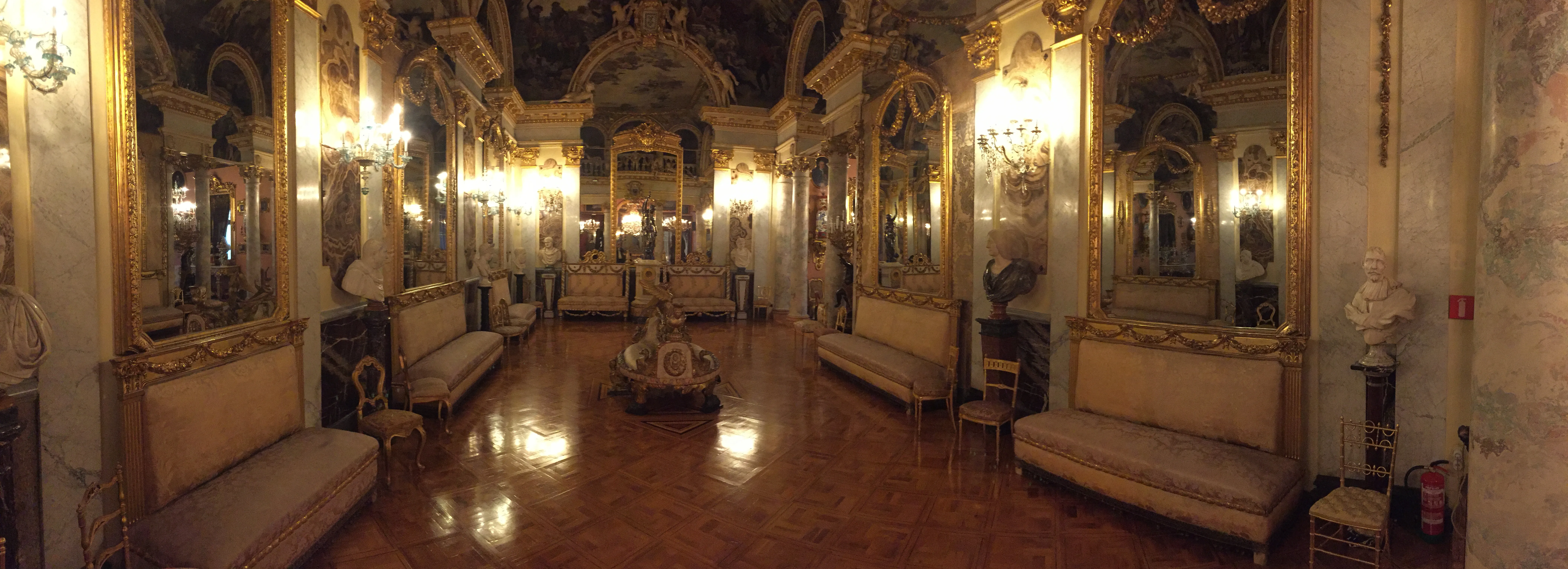Zdobna sala balowa ze złotymi lustrami, żyrandolami i ławkami