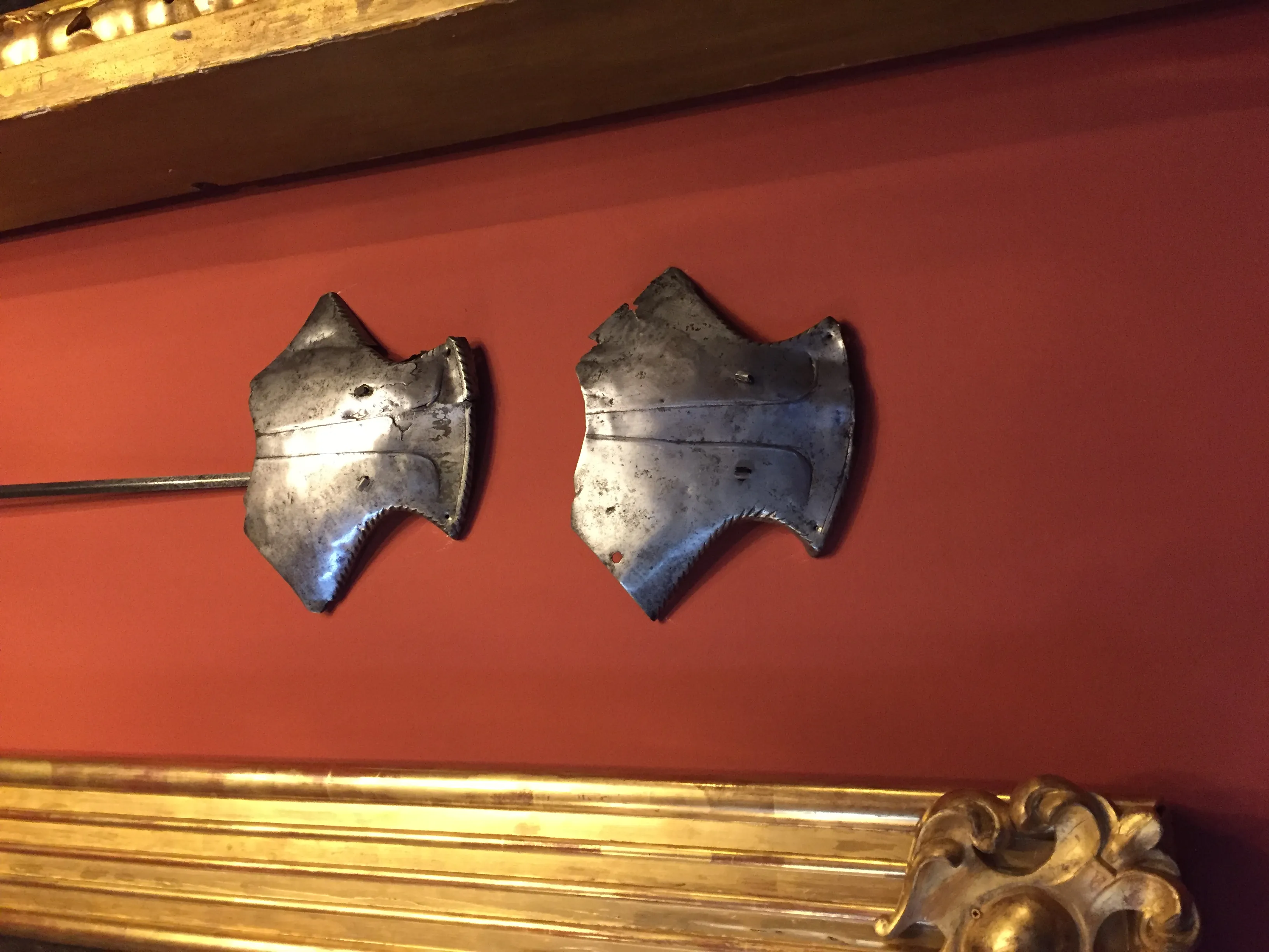 Dos piezas de armadura de metal montadas en una pared roja con un marco dorado debajo