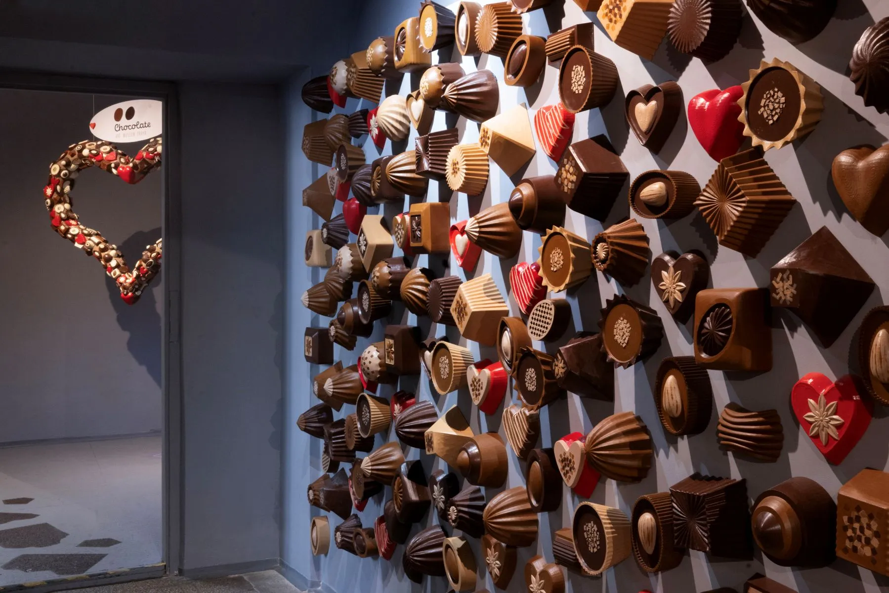 A wall covered with chocolate sculptures in various shapes and sizes, including hearts and molds, with a heart-shaped chocolate decoration on the left.