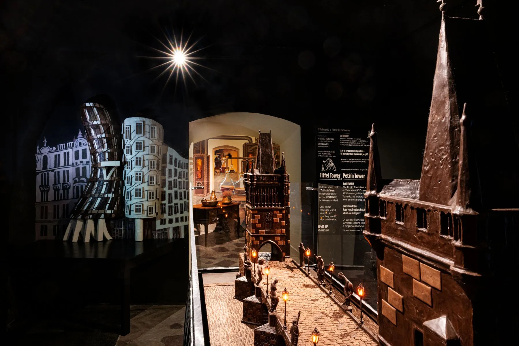Chocolate sculptures of buildings and a cityscape on display in a dimly lit museum exhibit