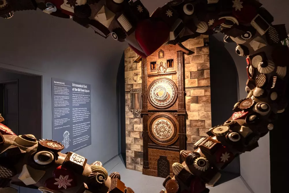 Chocolate art installation with a heart-shaped frame made of chocolate pieces surrounding a decorative wooden clock in a museum gallery