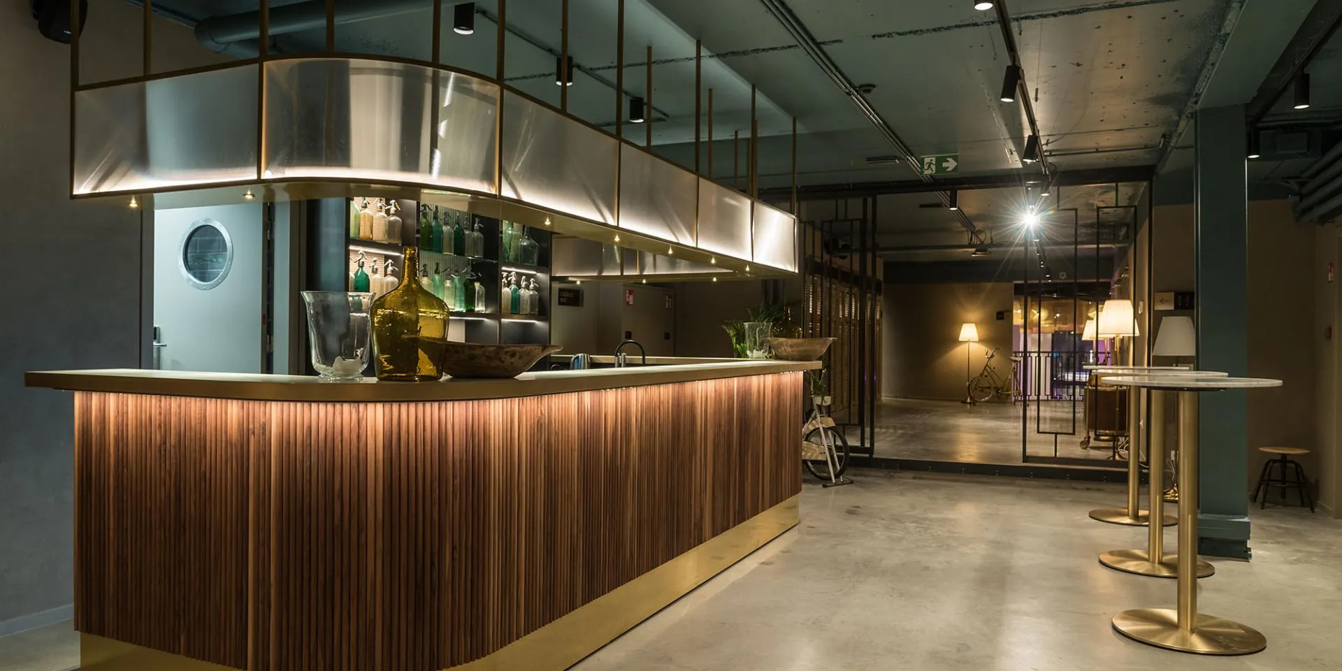Área de bar con mostrador de listones de madera, detalles en latón y una cálida iluminación ambiental en el interior del local.