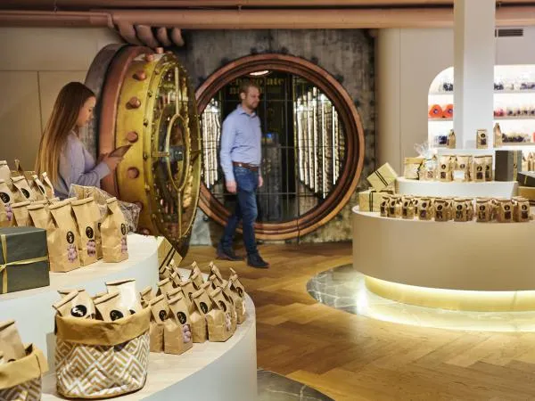 Interior de la tienda del museo Chocolate Nation con visitantes curioseando productos de chocolate expuestos en mostradores circulares blancos, con una gran puerta de bóveda circular decorativa al fondo.