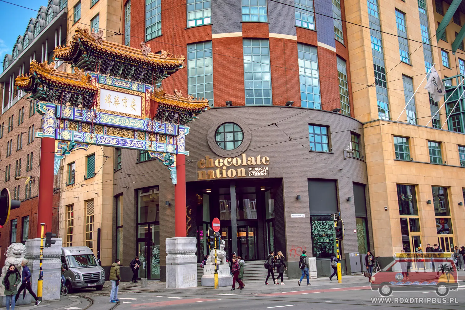 Vista exterior del edificio del museo Chocolate Nation con su letrero de entrada, junto a un arco tradicional chino en una calle de la ciudad con peatones