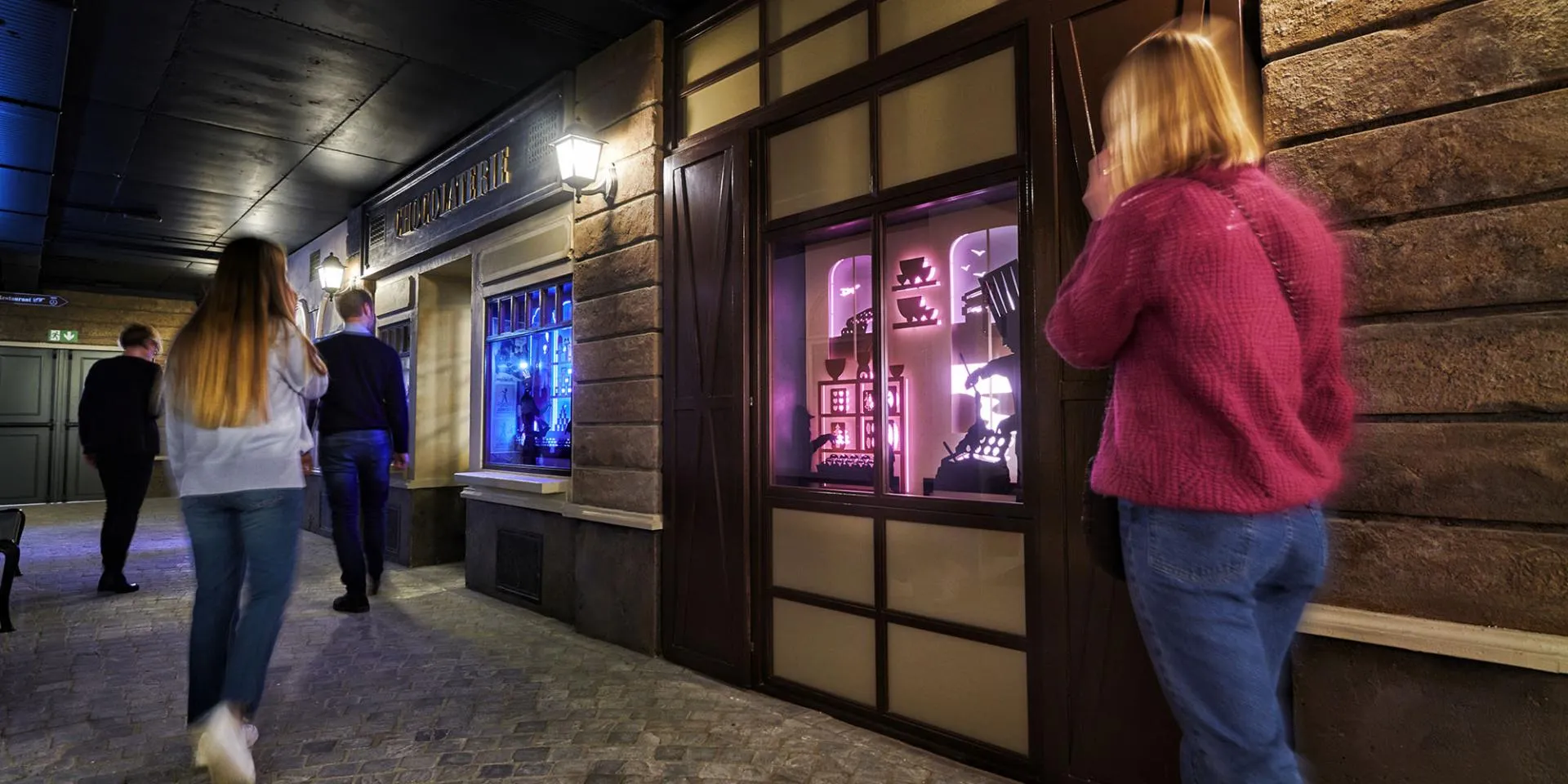 Los visitantes del museo caminan por un pasillo interior con fachadas de madera y escaparates iluminados que muestran exposiciones temáticas.