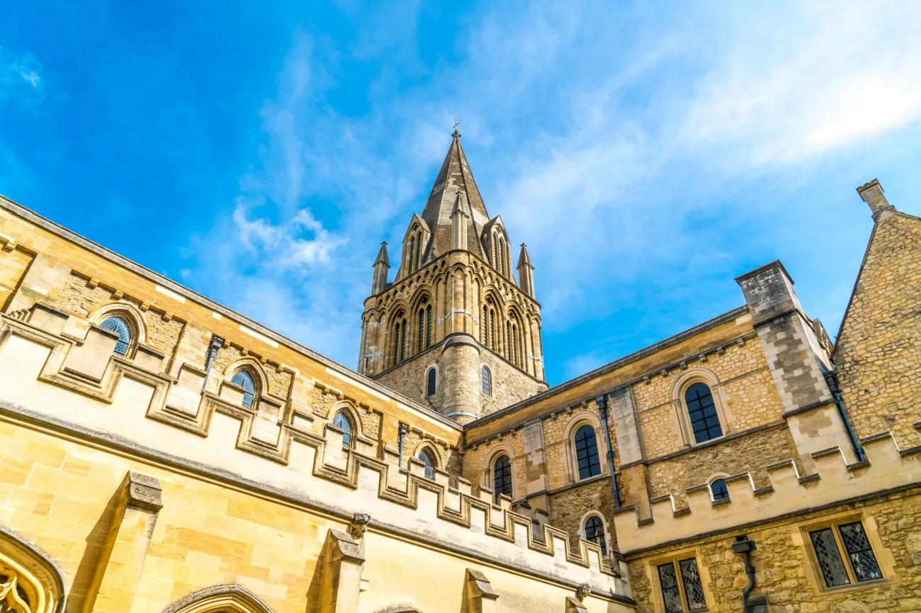 Wieża Tom Tower przy Christ Church Cathedral wznosząca się ponad średniowiecznymi kamiennymi budynkami na tle jasnobłękitnego nieba