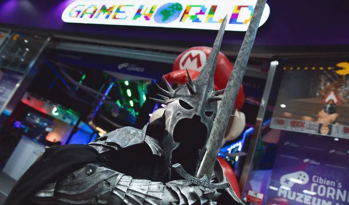 A person in a dark, spiky helmet and armor with a red Mario cap standing under a colorful 'GAME WORLD' sign