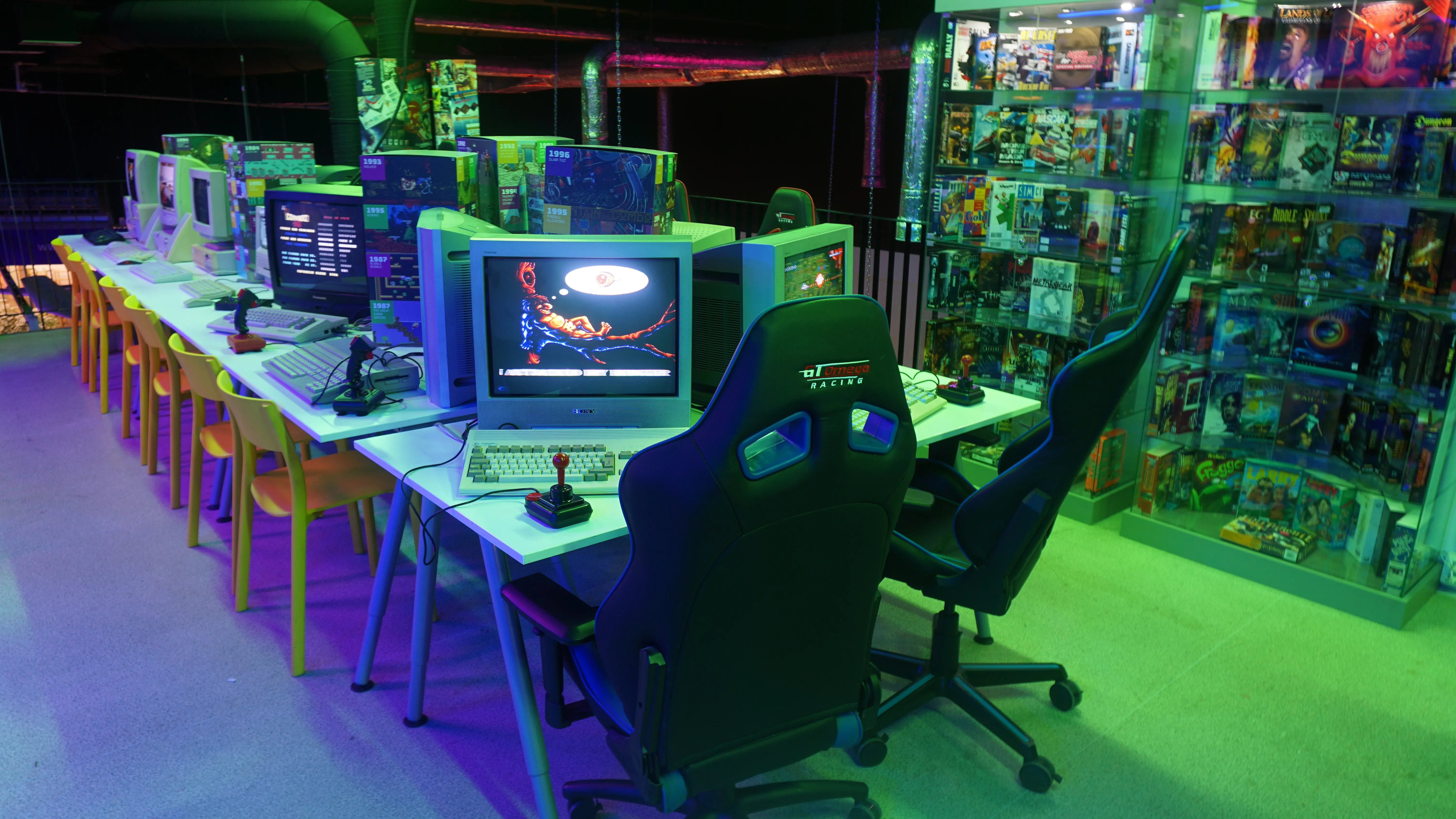 Rows of retro gaming stations with arcade machines and consoles under colorful neon lighting