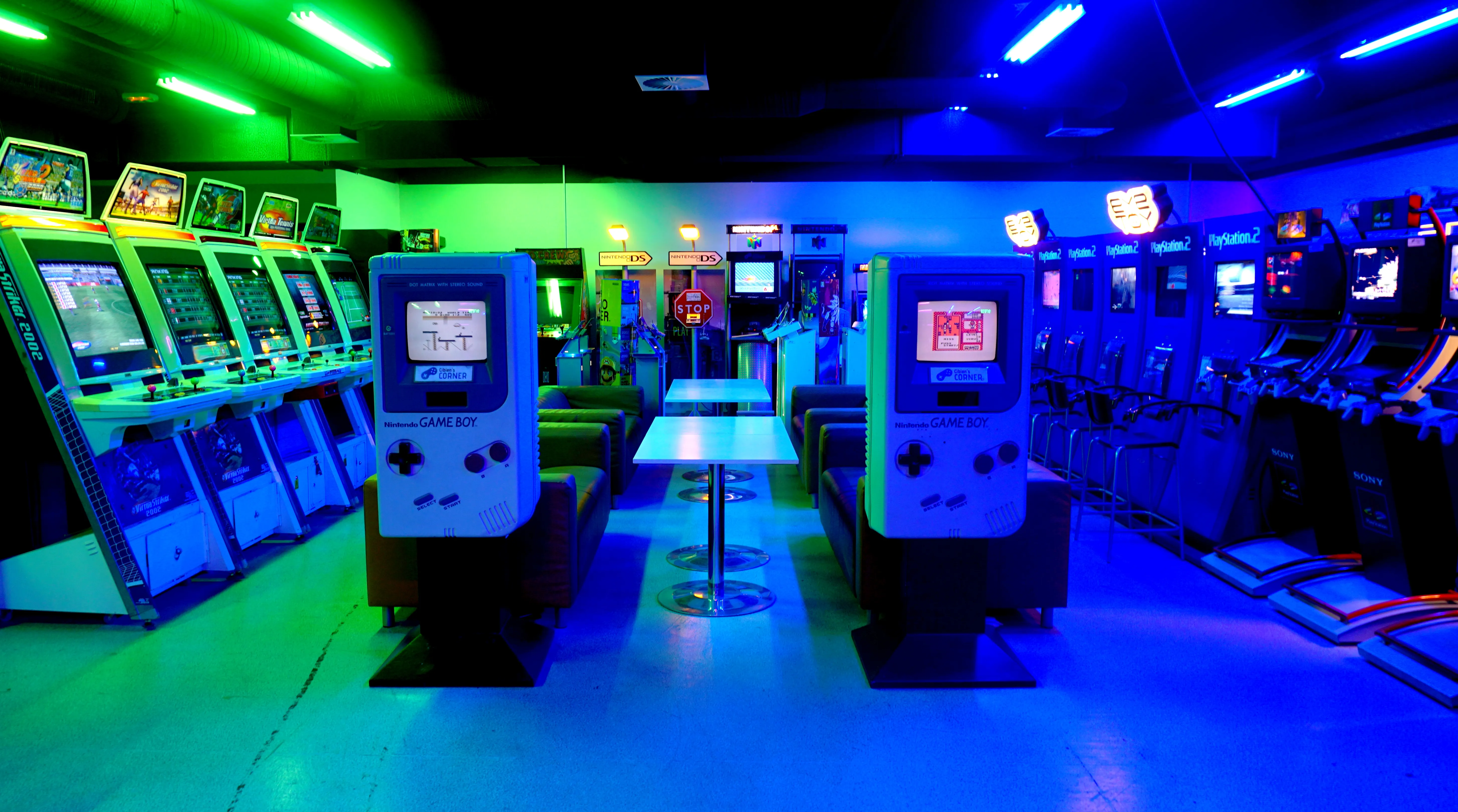 Rows of vintage arcade machines and handheld gaming consoles under green and blue neon lighting in a museum interior