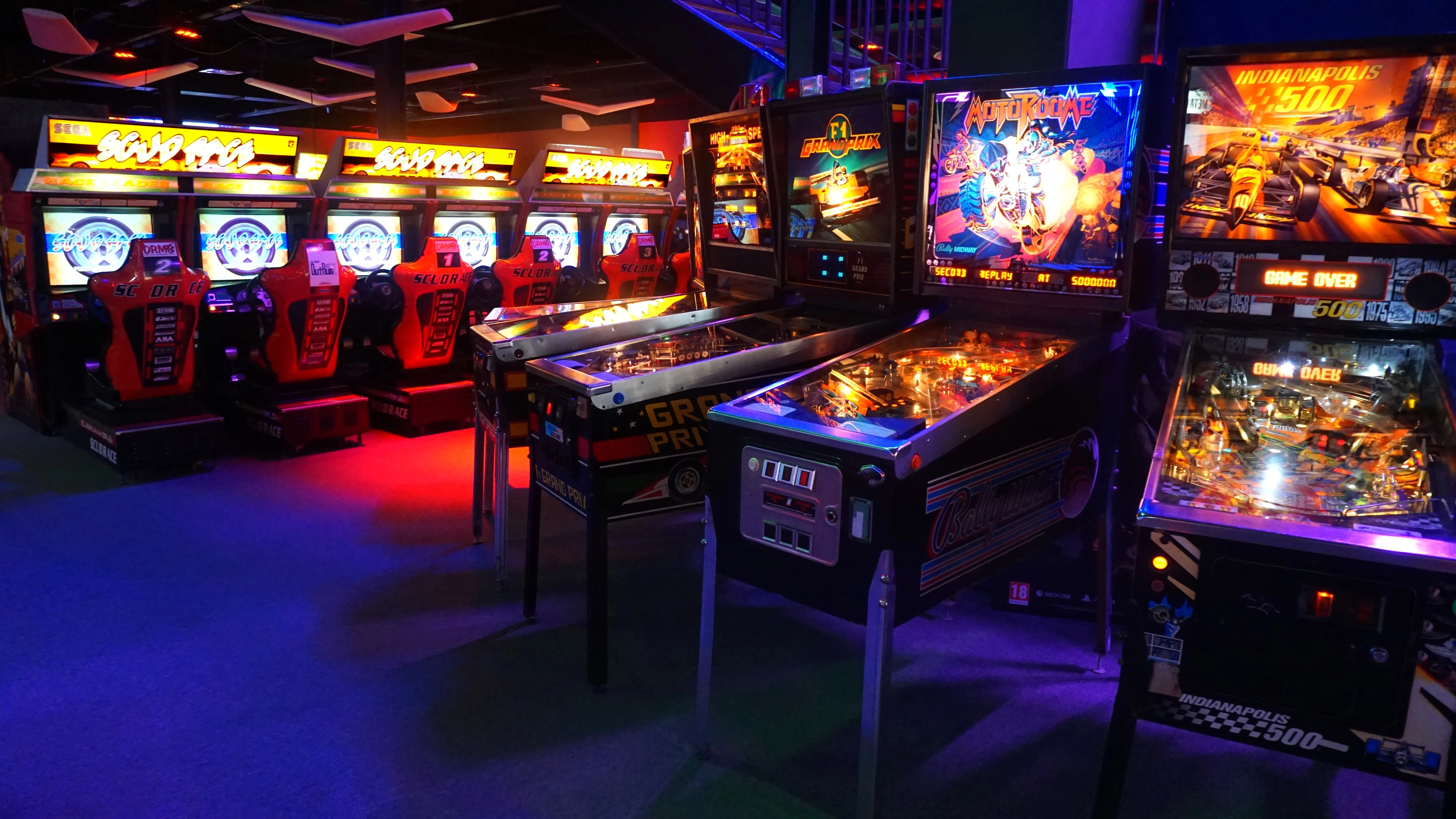 Arcade machines and pinball tables in a dimly lit room with vibrant neon lights