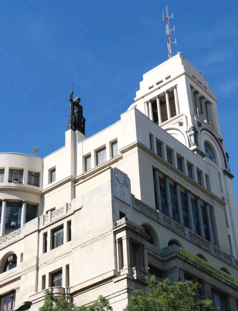 Beige Art Deco building with a statue on the roof and arched windows under a blue sky