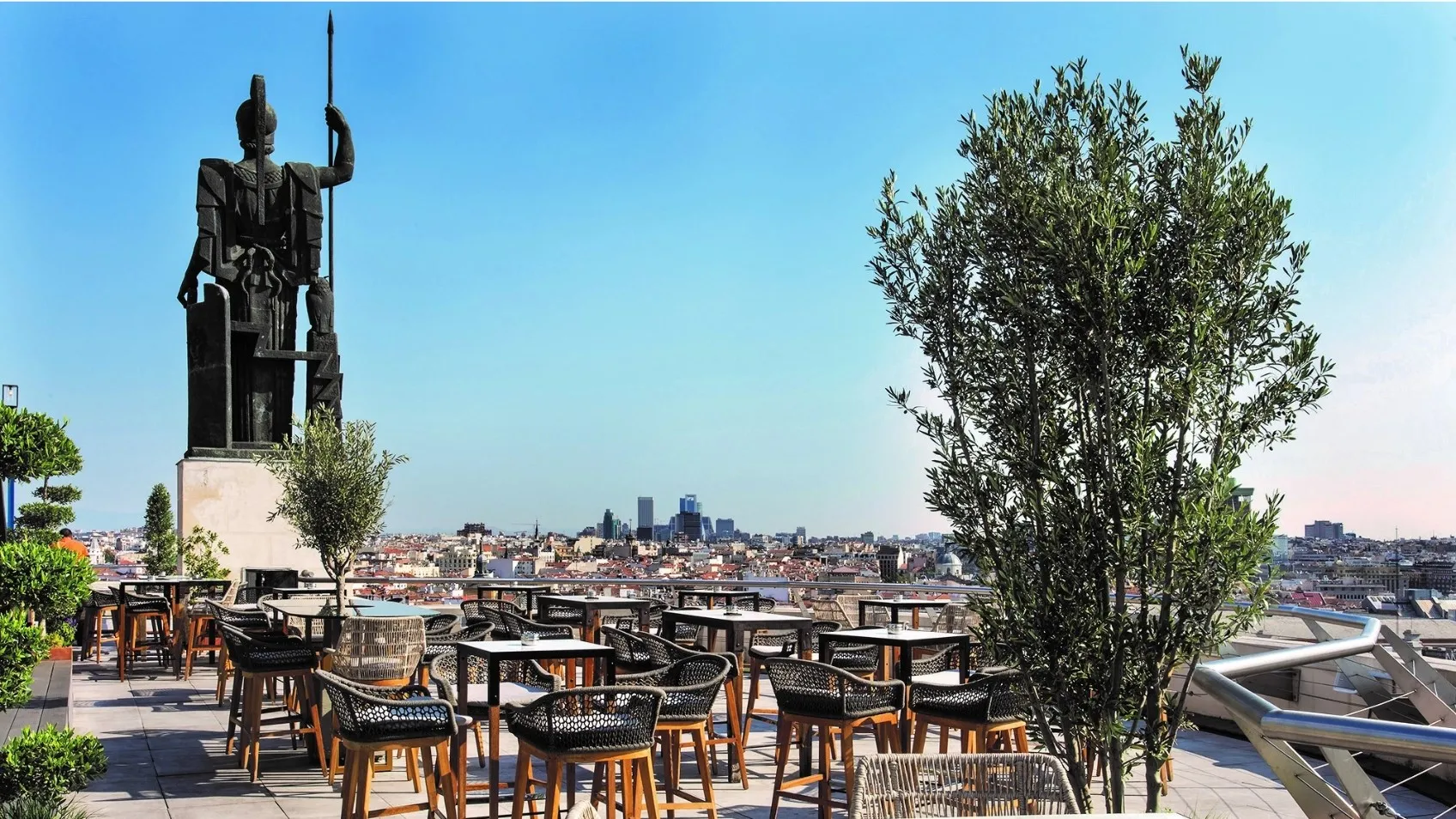 Rooftop terrace with tables and chairs, a large statue, and a cityscape view of Madrid under a blue sky