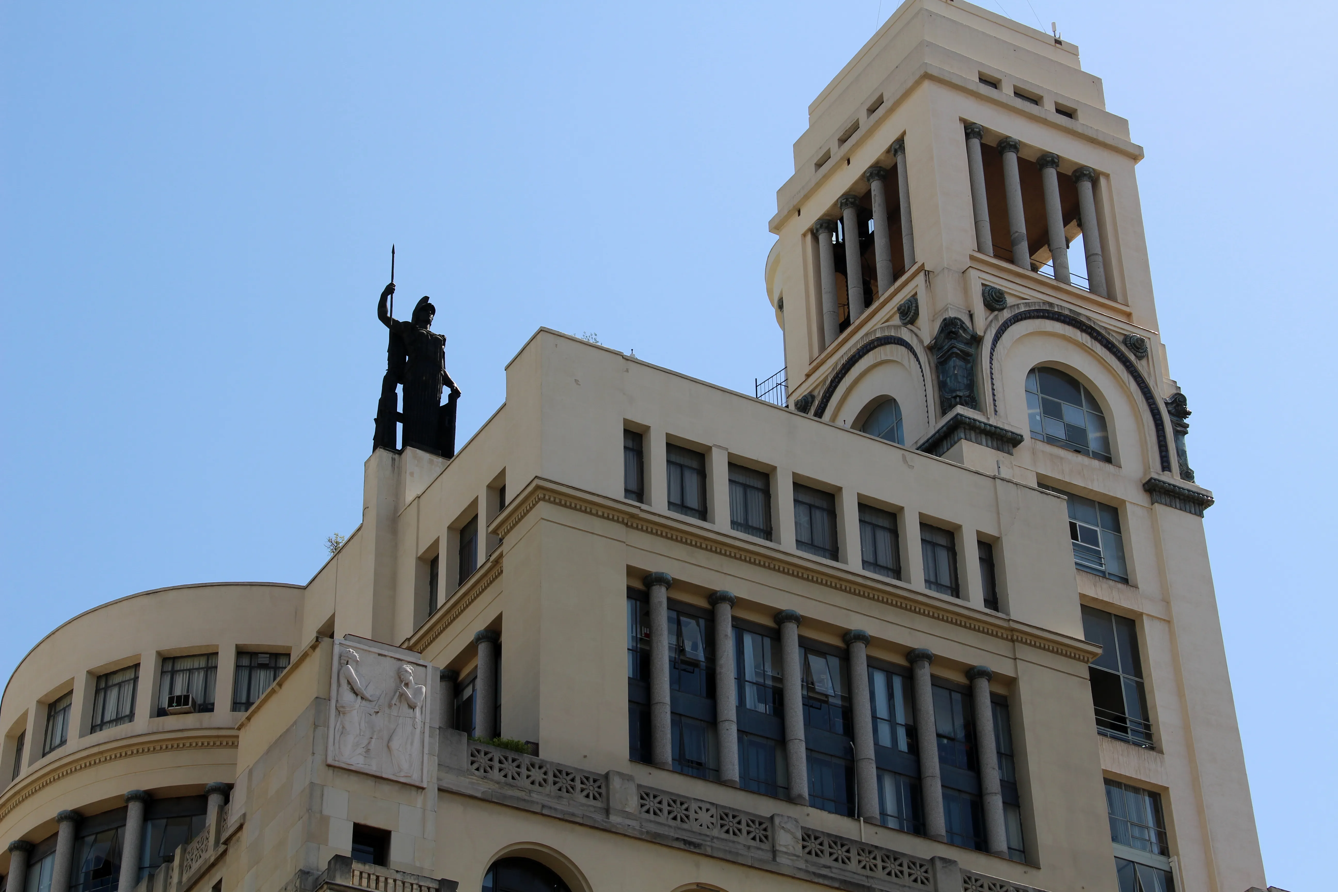 Beige building with a tall tower and a statue on the roof against a blue sky
