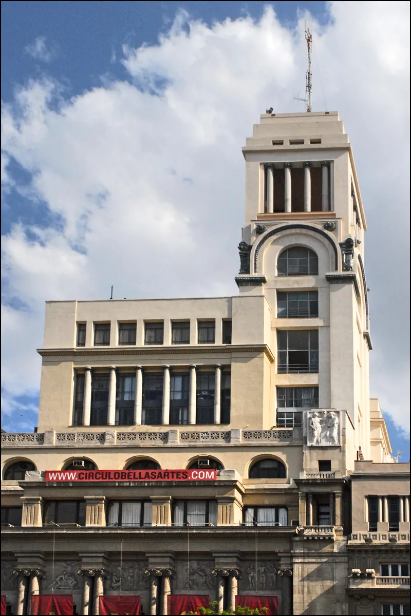 A tall, ornate building with classical columns and a tower, featuring a red sign with the text 'WWW.CIRCULOBELLASARTES.COM' on the facade, under a blue sky with white clouds.