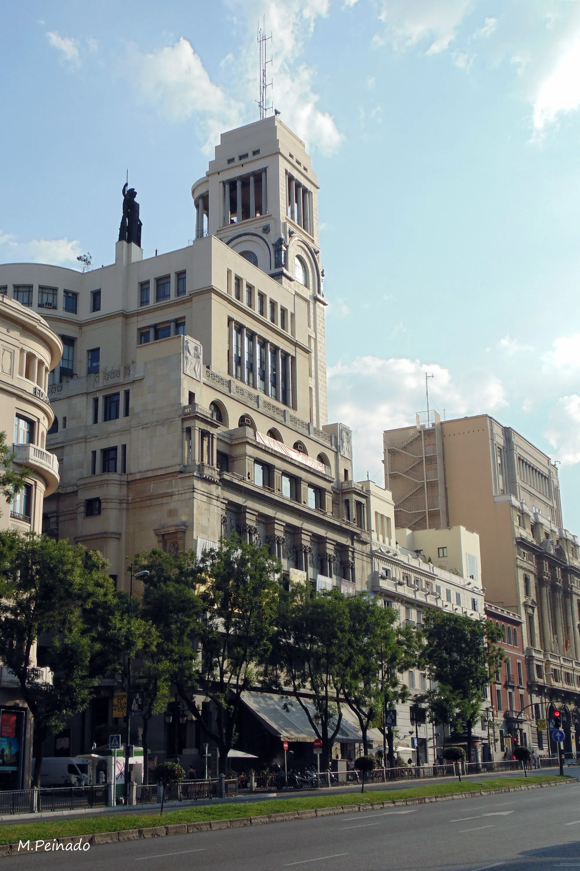 The Círculo de Bellas Artes building with its beige facade, arched windows, and a statue on the roof, surrounded by trees and a street in Madrid.