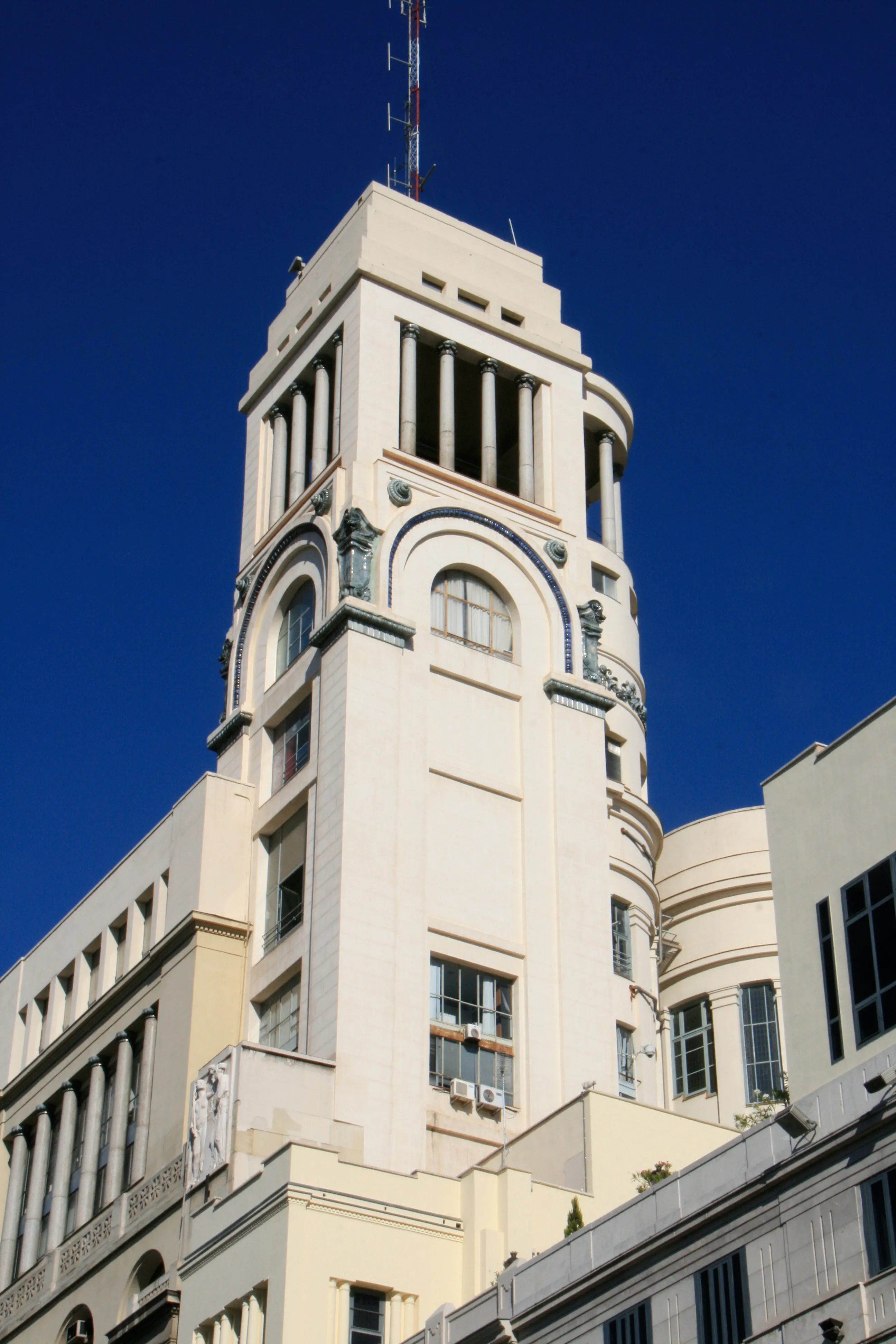 Beige building with classical architectural details and a tower against a blue sky