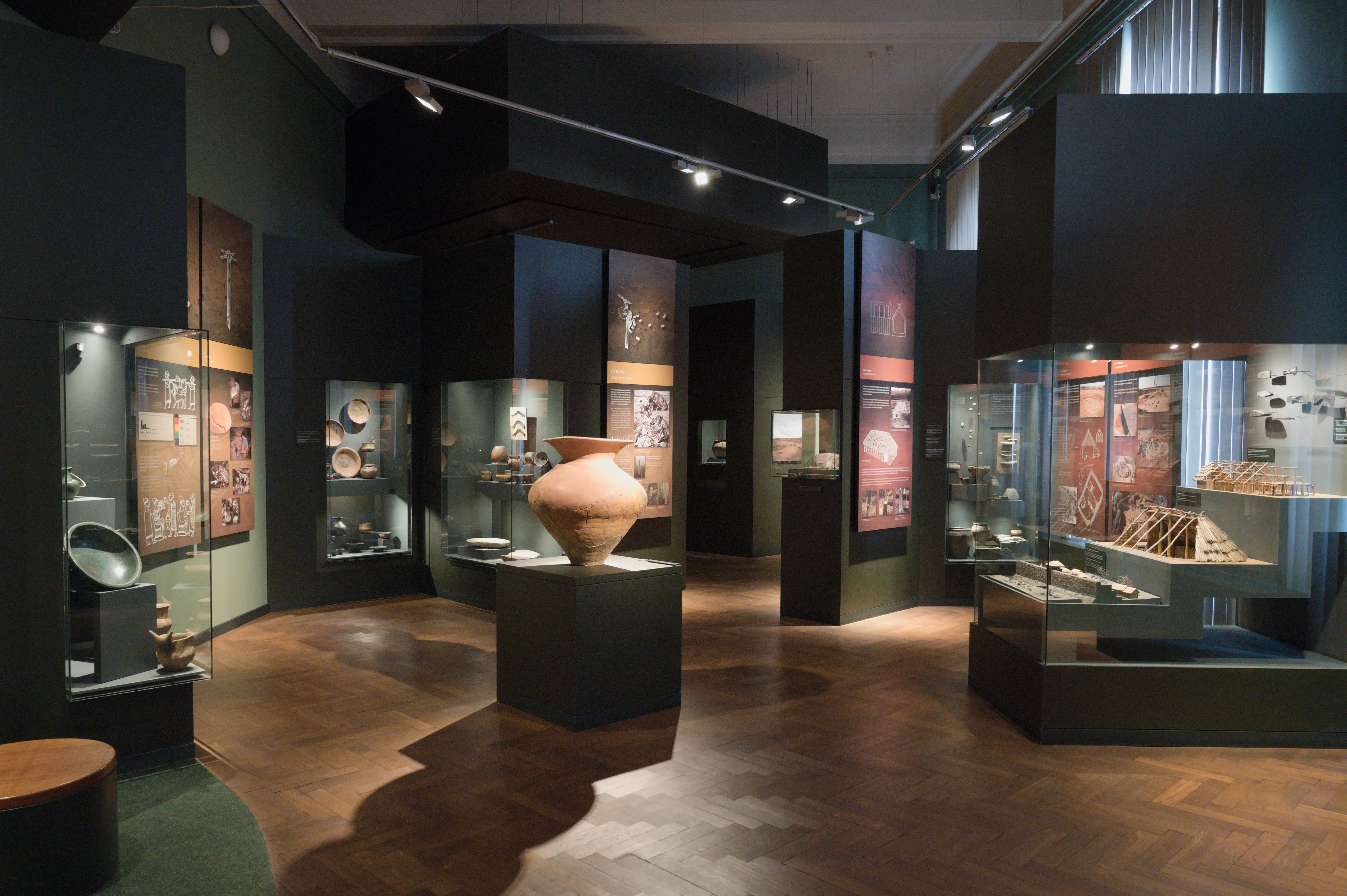 Spacious museum gallery with wooden floors, dark walls, and glass display cases containing historical artifacts