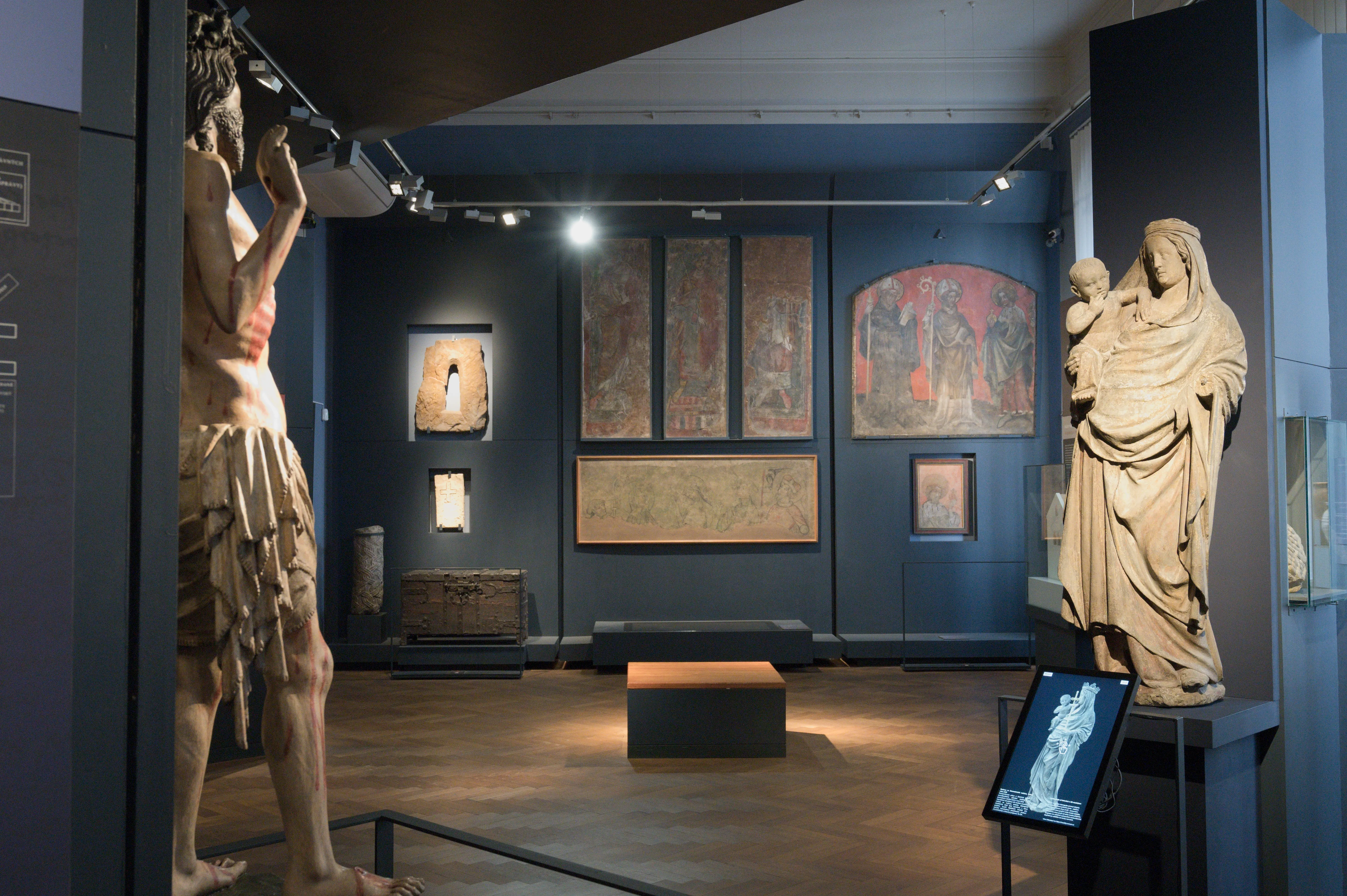 Interior of the City of Prague Museum with two large statues and framed artworks on display