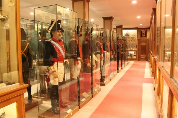 Een rij vitrines in een museumhal, elk met een paspop gekleed in een historisch uniform van de Spaanse Burgerwacht.