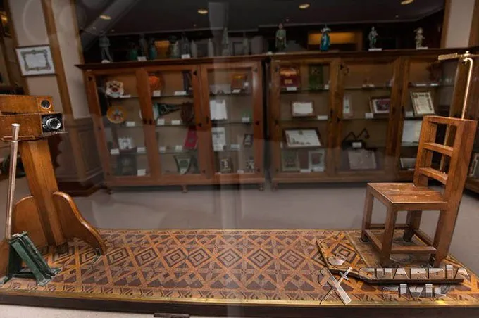 Tentoonstelling met een houten stoel, camera en andere historische artefacten in een vitrine