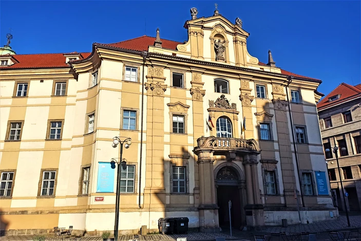 Edificio de estilo barroco con fachada ornamentada, tejado rojo y entrada central bajo un cielo azul