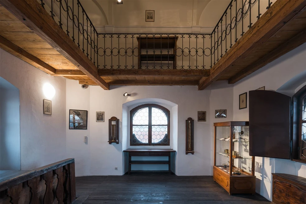 Interior de una biblioteca histórica con barandillas de madera, ventana arqueada y vitrina
